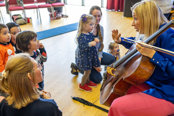 Woman with cello playing and chatting with small children 