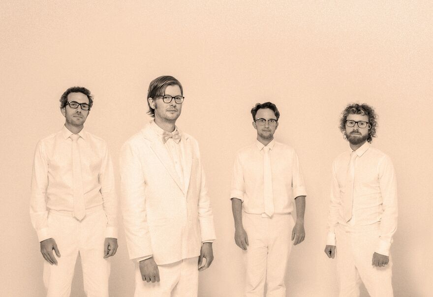Light pink washed photo of four men wearing white suits and ties