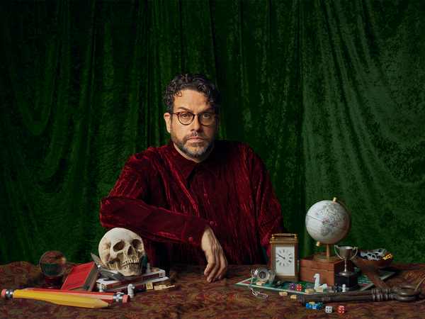 Man sat in a dark red shirt leaning on a skull 