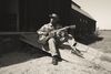 Eric Bibb sat on a ramp outside a building playing guitar, image is in black and white