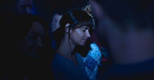 A young woman closes her eyes as she is surrounded by people. 