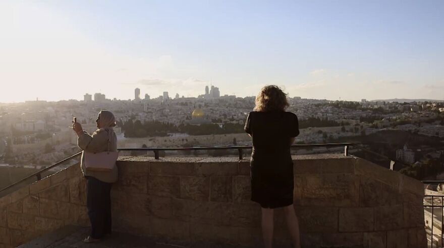 Two people stand at the top of stone steps taking photos of the city below. 