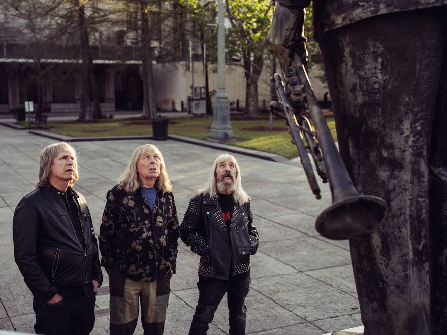 The members of Spinal Tap look up at a statue.