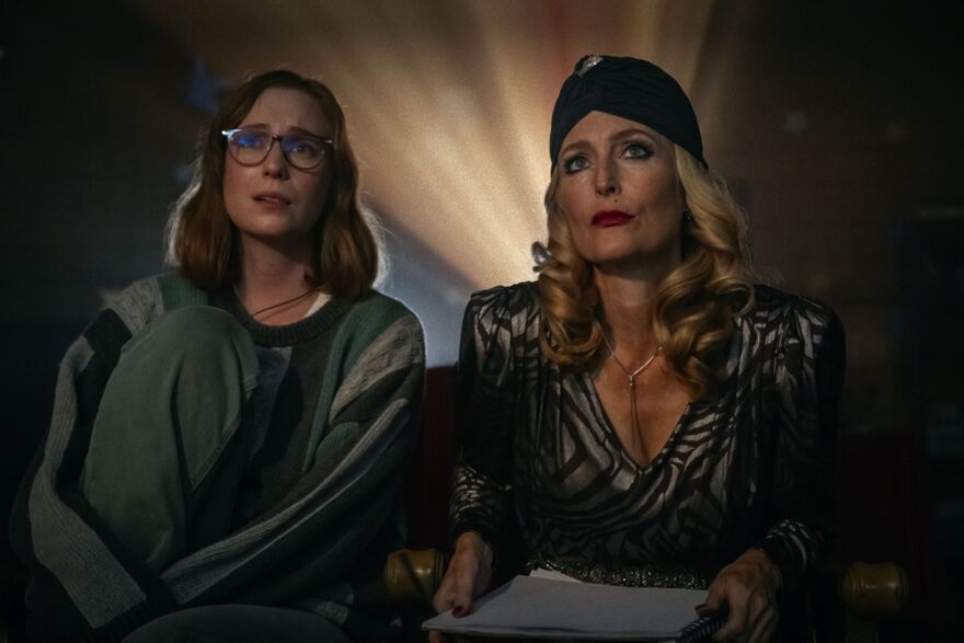 Two women watching a film. The younger woman wears leisure clothing whilst the older woman wears old Hollywood glamour. 