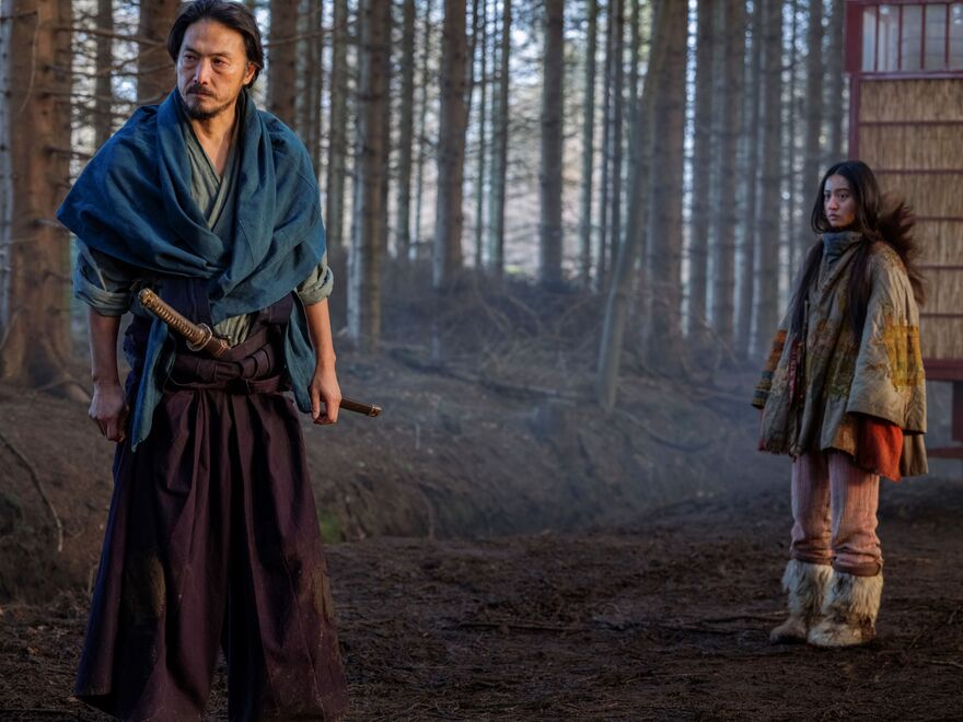 A Samurai stands in a woodland with his daughter stood behind.