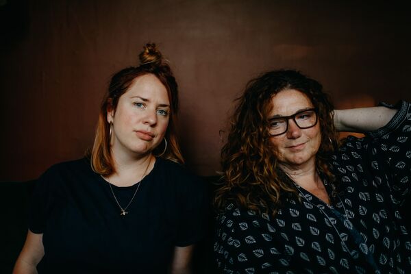 Sara Colman and Rebecca Nash sat in front of a dark brown wall