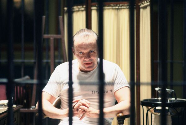 A man dressed in all white sits in a locked cell. 