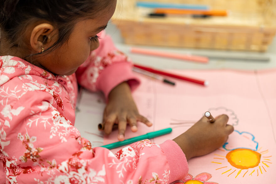 Young girl drawing on pink paper