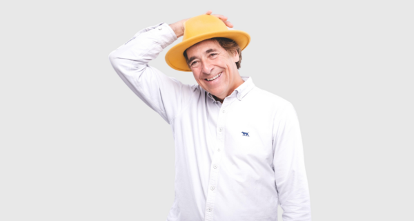 Mark Steel standing holding a yellow hat on his head