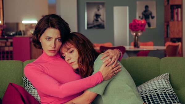 Two women share an embrace on a green sofa. One is comforting the other. 