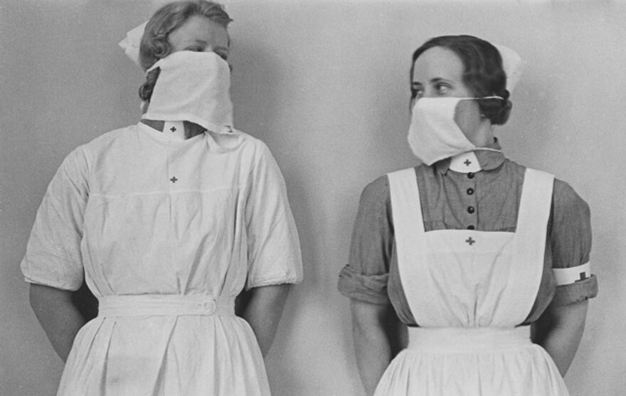 A black and white photo of two old fashioned nurses with large face coverings
