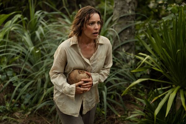 A scared and dishevelled looking woman walks through a jungle. 