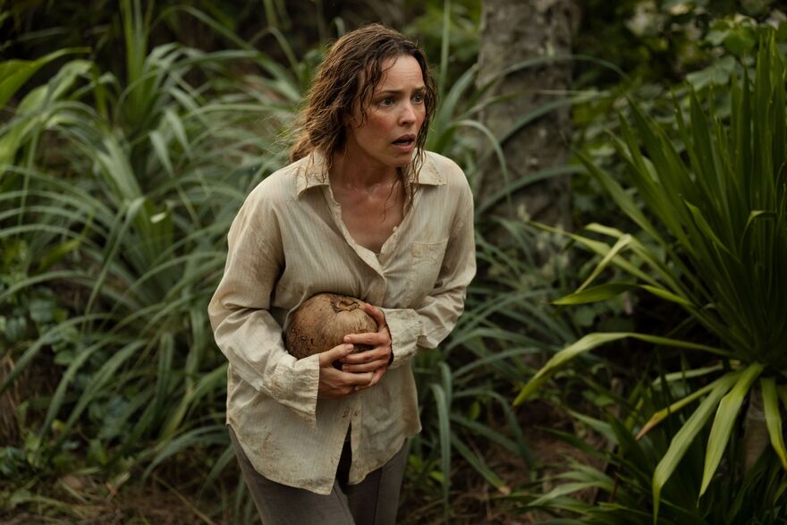 A scared and dishevelled looking woman walks through a jungle. 