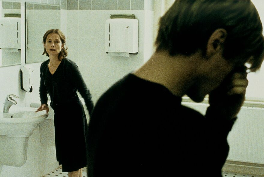 A woman stands against a bathroom sink looking over a man with his head in his hands. 