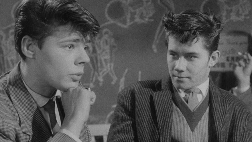 A black and white photo of two young men in conversation. 