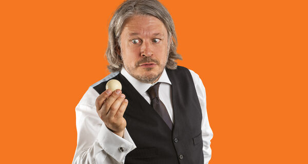 Richard Herring holding a white ball in front of an orange background