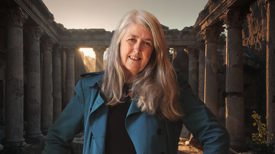 Mary Beard smiling with roman ruins behind her