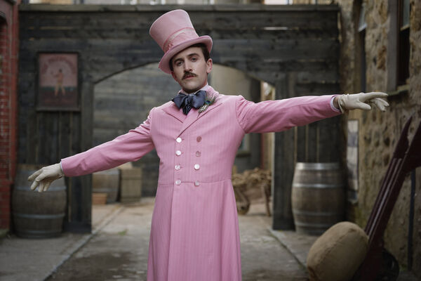 A man stands with his arms out wearing a pastel pink suit. A man stands with his arms out wearing a pastel pink suit.