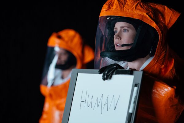 A woman in an orange hazmat suit holds up a whiteboard that says 'Human'. 