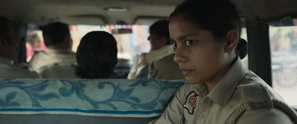 A young woman in a police uniform sits in the back of a car. 