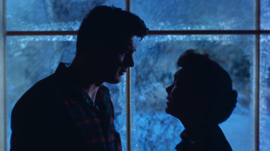 A man and woman face each other in the near darkness.