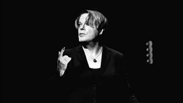 Black and white image of Eddie Izzard speaking on stage