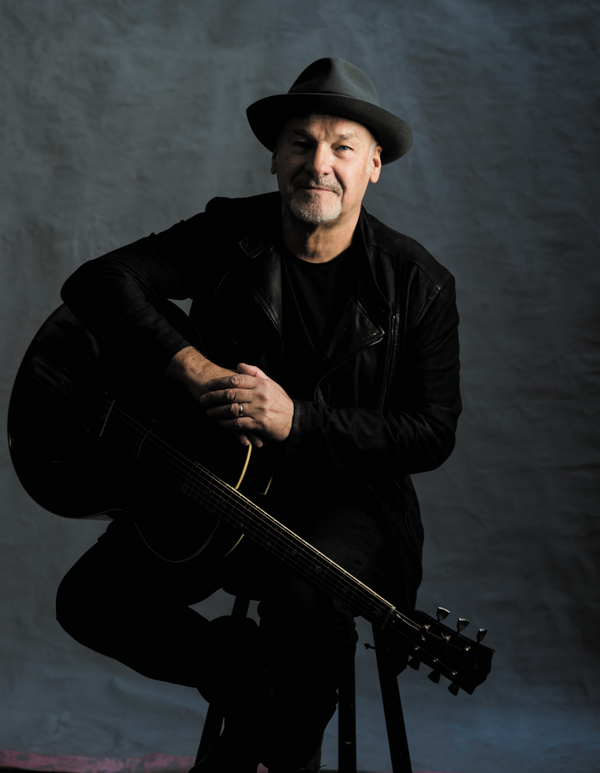 Man in a black suit and hat sitting on a stool holding a guitar