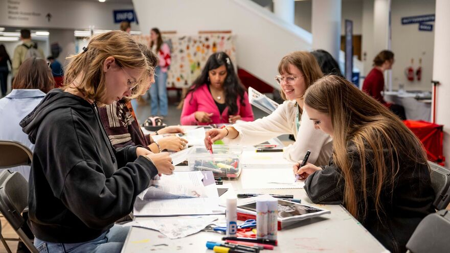 Students gathered at a workshop table making crafts with paper, glue, and markers.
