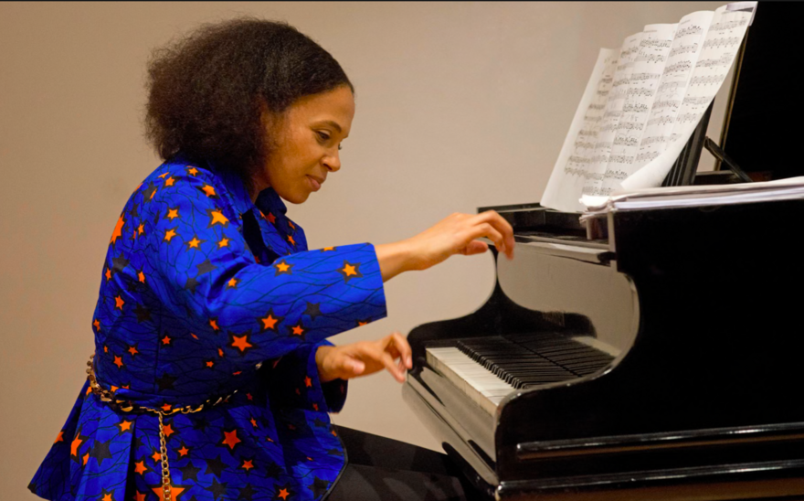 Pianist Rebeca Omordia in a blue gown, seated at a black grand piano.