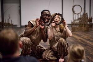 Two dancers kneeling holding weaved circles over face