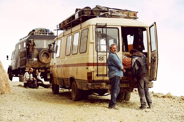 Two camper vans next to each other on a dusty road. Two men can be seen next to each vehicle. 