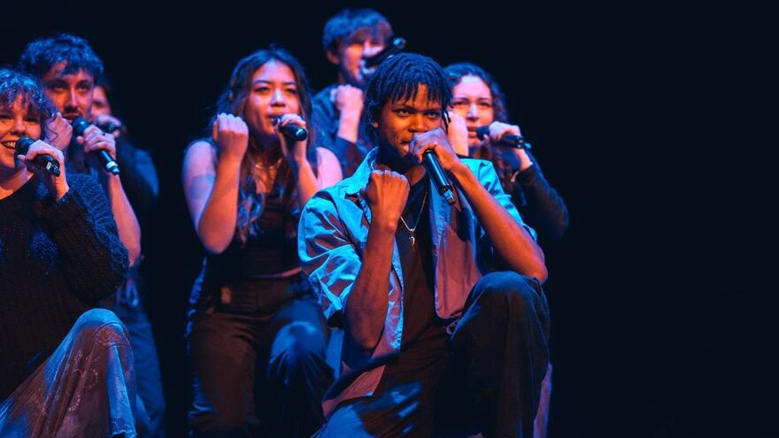 A stage shot of an a cappella group performing under blue and purple lighting.