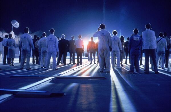 A large group of people look towards a beaming light. 