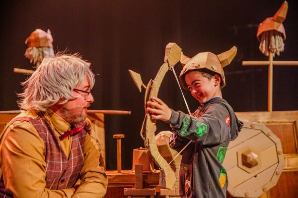 Young boy in a viking helmet with a bow and arrow next to a man with long grey hair
