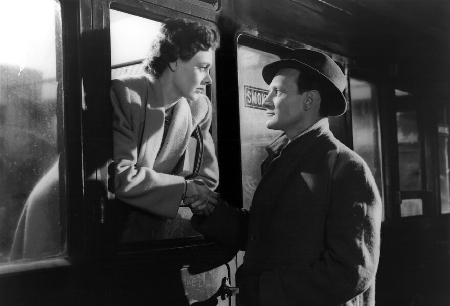 A woman leans out of train window looking into the eyes of a man outside who is looking back at her