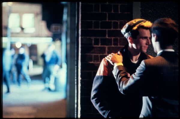 Two men stand together in an alley. 