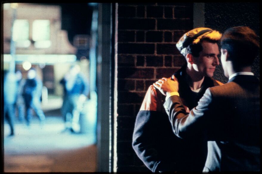 Two men stand together in an alley. 