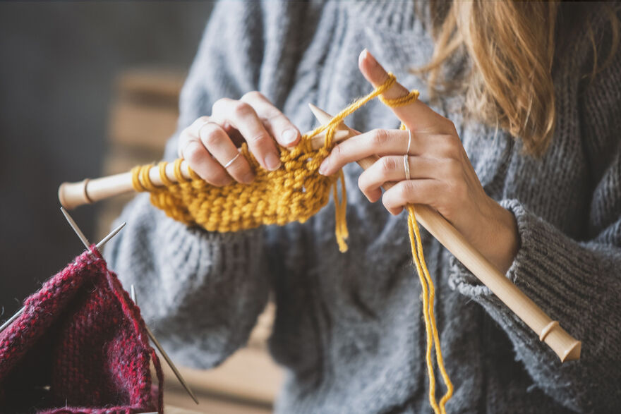 Hands holding knitting needles and knitting a yellow garment