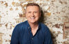 Aled Jones standing in front of an exposed brick wall smiling