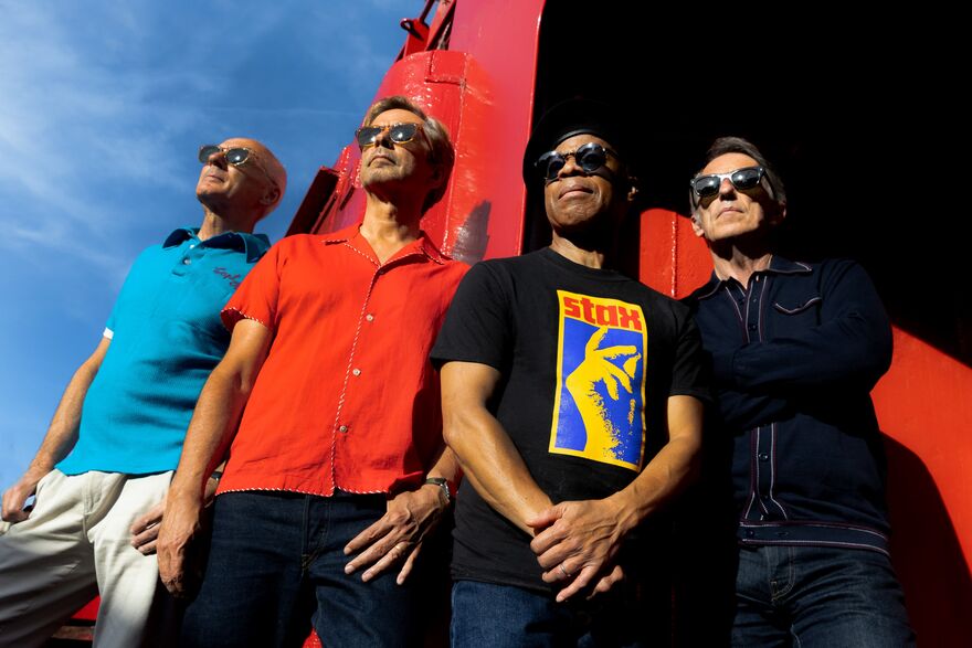 4 men in sunglasses stood against a red building