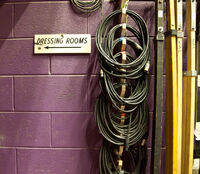 Purple breeze block wall with dressing room and arrow sign, and cables coiled up and hanging from the wall