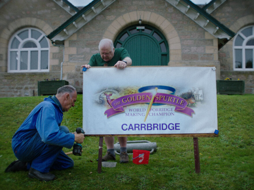 Two men put up a sign for The Golden Spurtle World Porridge Making Championships.