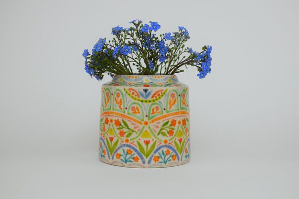A colourful clay pot with blue flowers inside