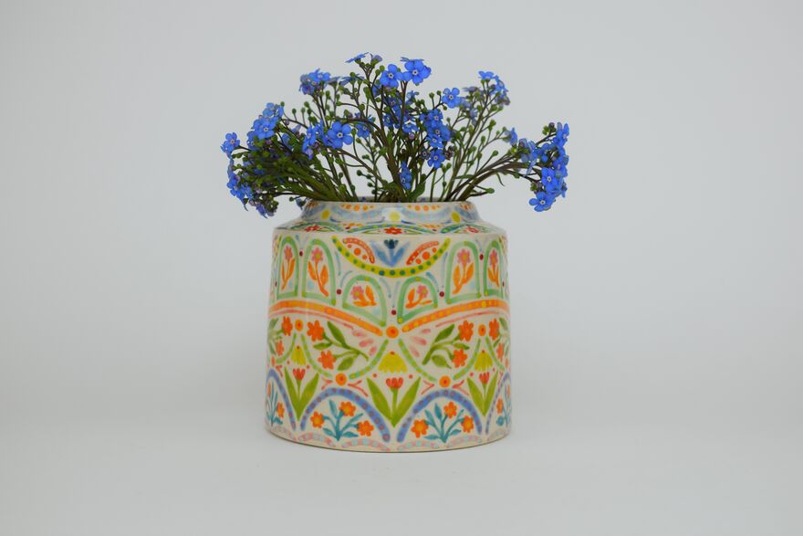 A colourful clay pot with blue flowers inside