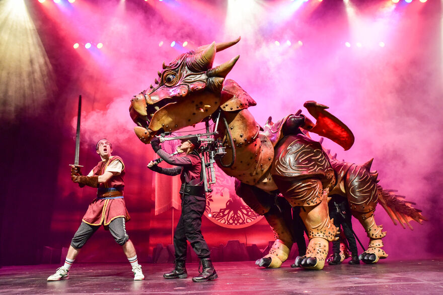 Man holding sword with a large dragon puppet on stage