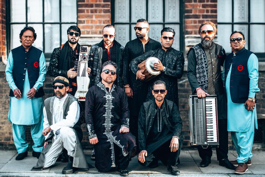 Band against brick wall, some standing with instruments and some kneeling