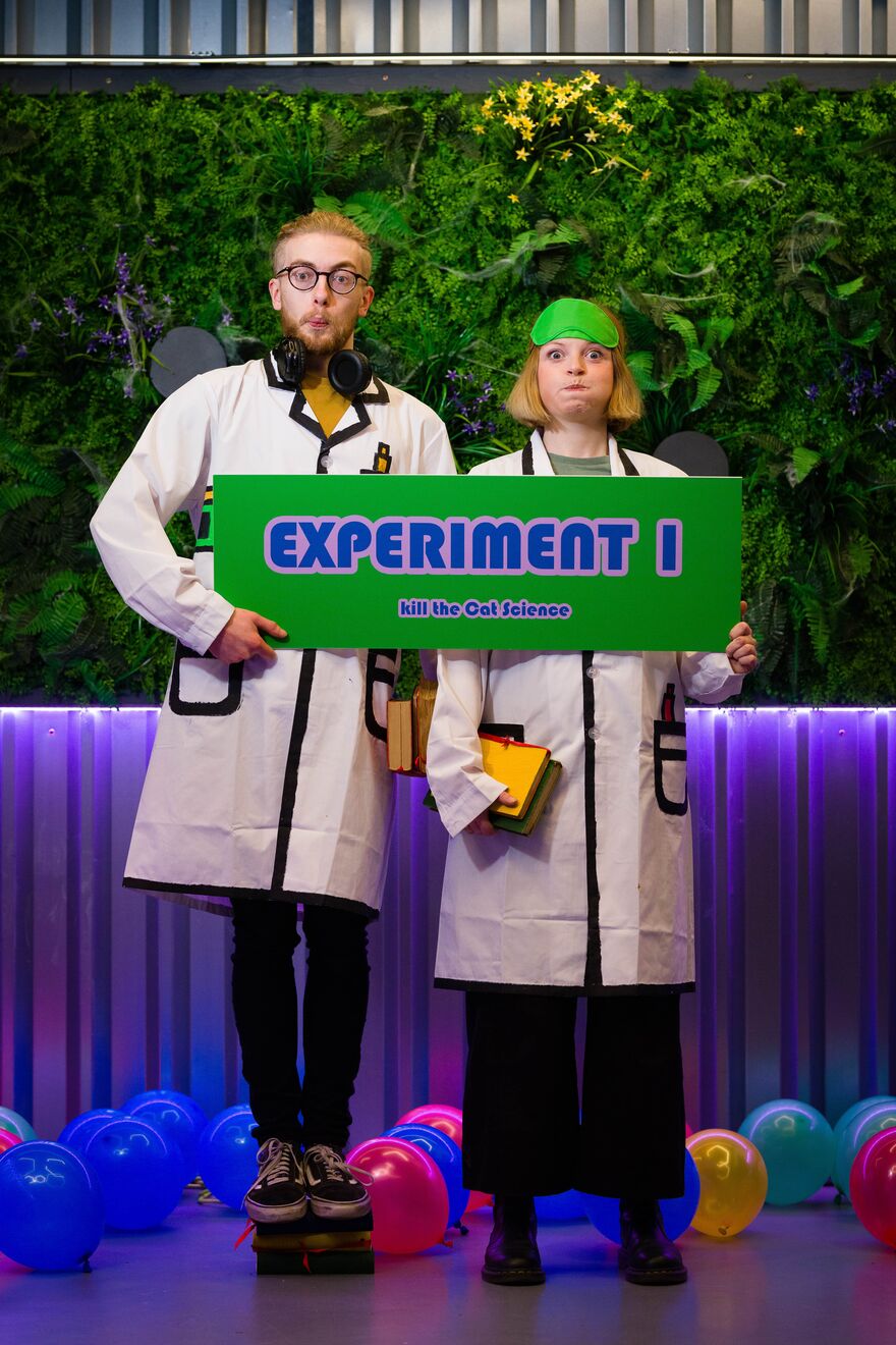 Man and woman wearing lab coats holding a green sign that says