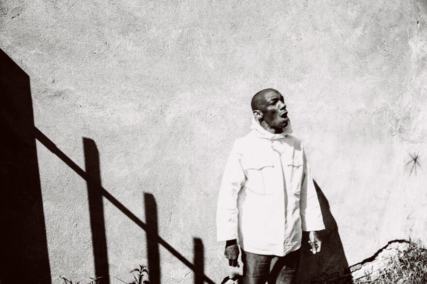 A man against a plain wall and the shadow of a fence
