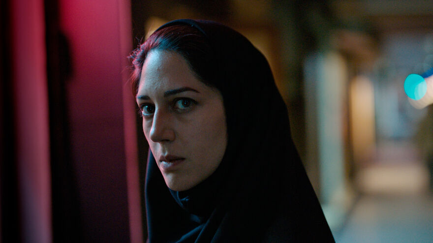 A woman wearing a head covering looks intently straight to camera.