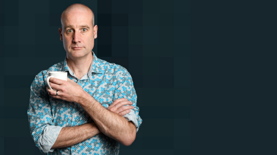 Matt Parker with his arms folded holding a white mug